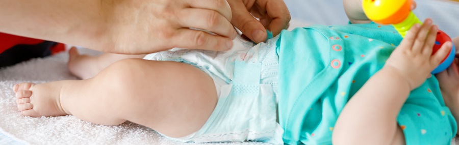 Close-up of father changing diaper of his newborn baby daughter. Little child, girl on changing table in bathroom with rattle toys.
