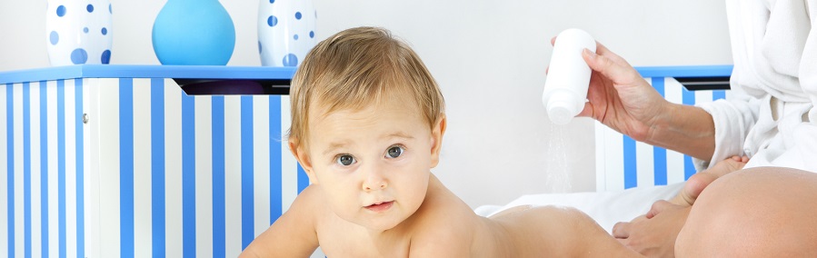 Mother pampering her baby girl daughter at home, applying baby powder to her body. Real people, mother 30-35, baby girl 10 months.